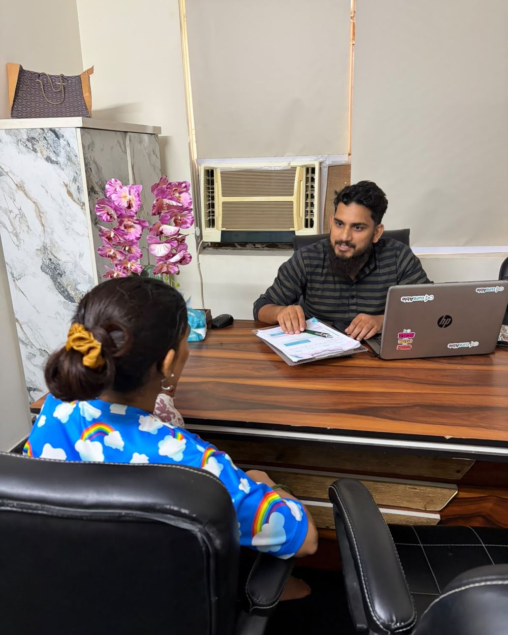 A child and an adult meeting a CureAble counsellor at his desk.