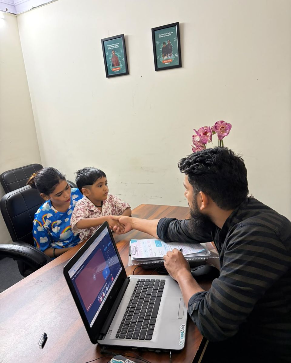 A CureAble counsellor talking with two children and an adult at his desk.