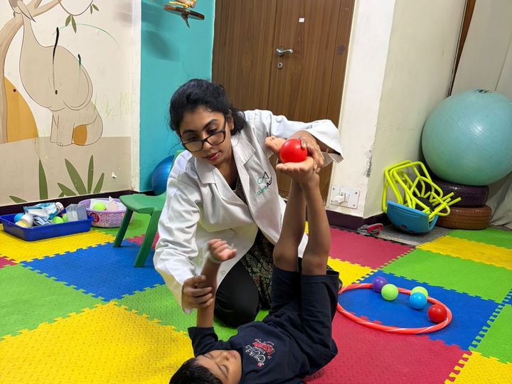 An occupational therapist guiding a child through a leg exercise on a play mat.