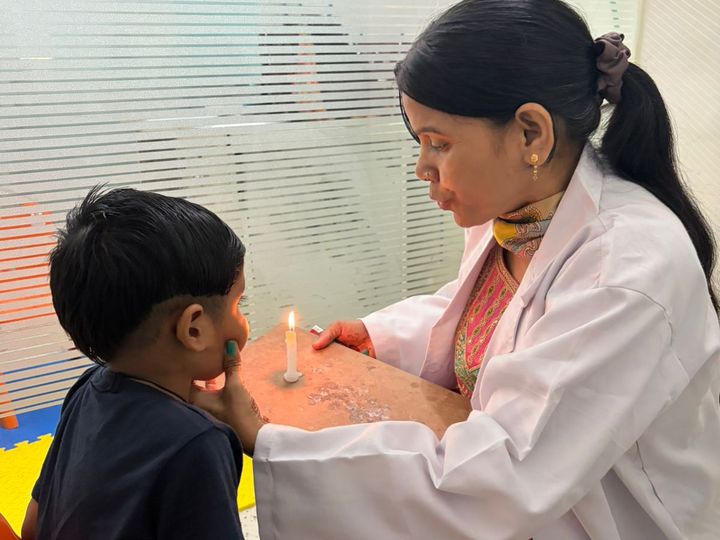A speech therapist and a child sitting across from each other beside a lit candle.