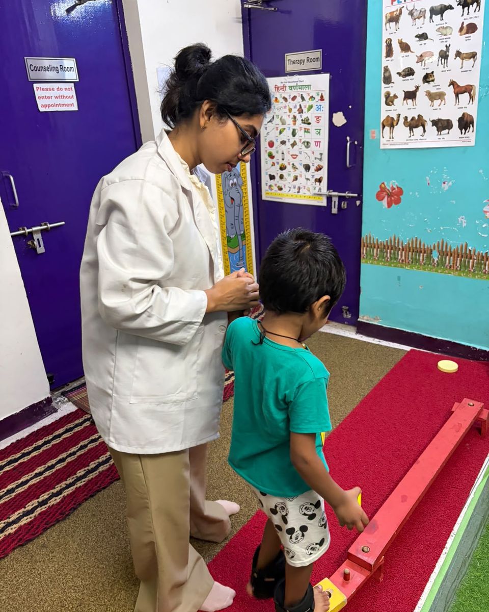 A therapist standing beside a child as they walk along a balance beam.