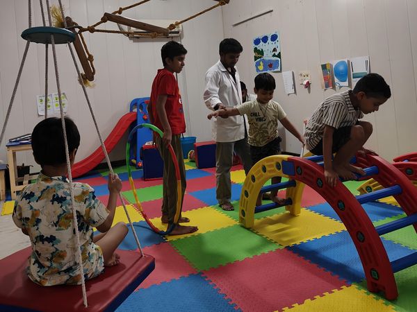 Children using the swing, ladders and climbing arches in the therapy room.