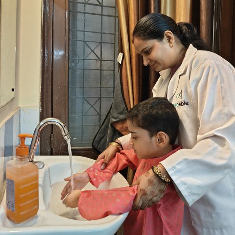 A child washing their hands at a basin with a therapist beside them.