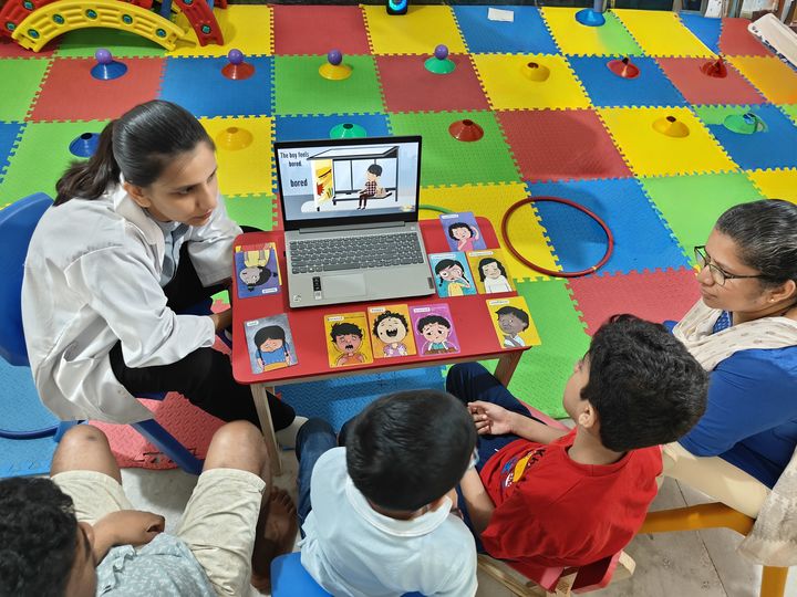 Two therapists leading a group of children through an emotions activity with picture cards.