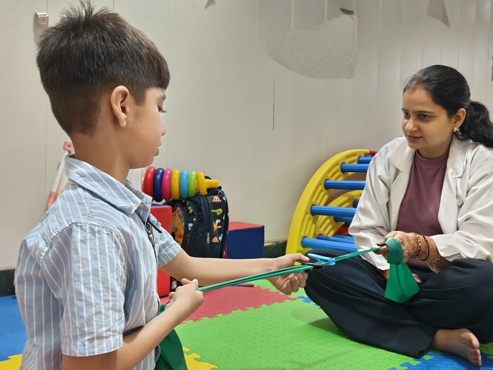 A child holding a resistance band during an occupational therapy session on a play mat.