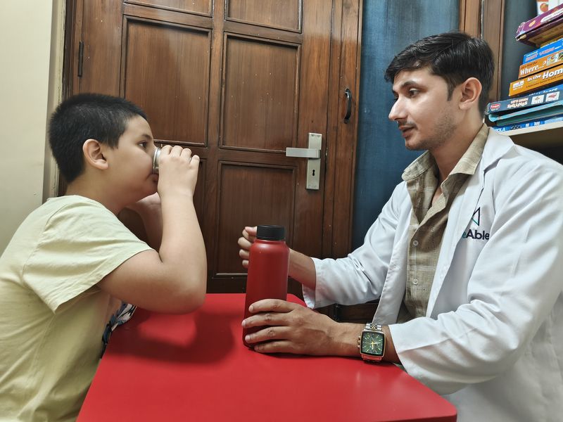 A child drinking from a water bottle at a table with a therapist.