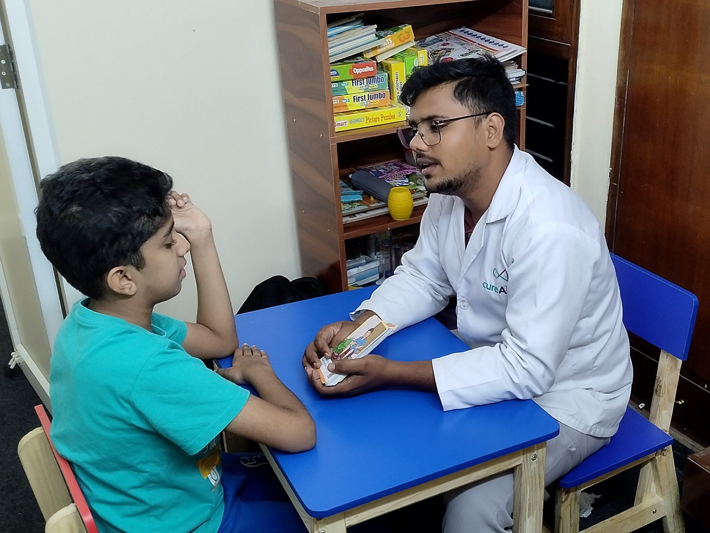 A CureAble child development expert talks with a child across a desk at the Noida Centre.