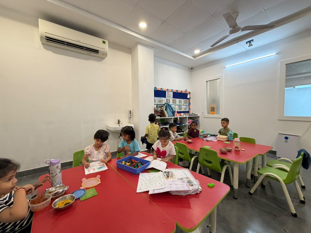Children working at low red tables with their teachers in a bright Early On classroom.