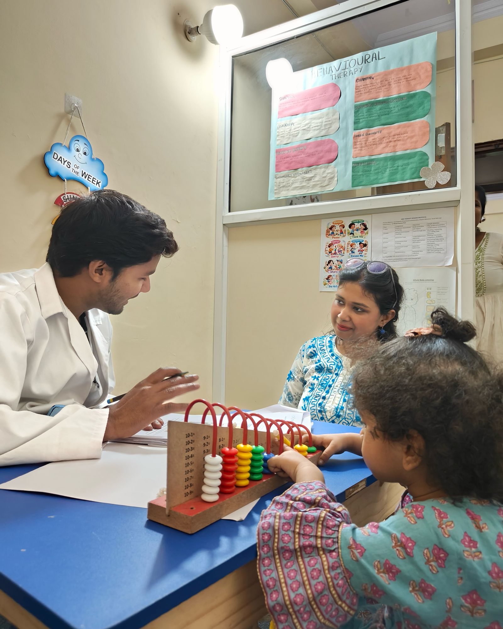 A therapist, an adult and a child working with an abacus at a table in a CureAble therapy room.