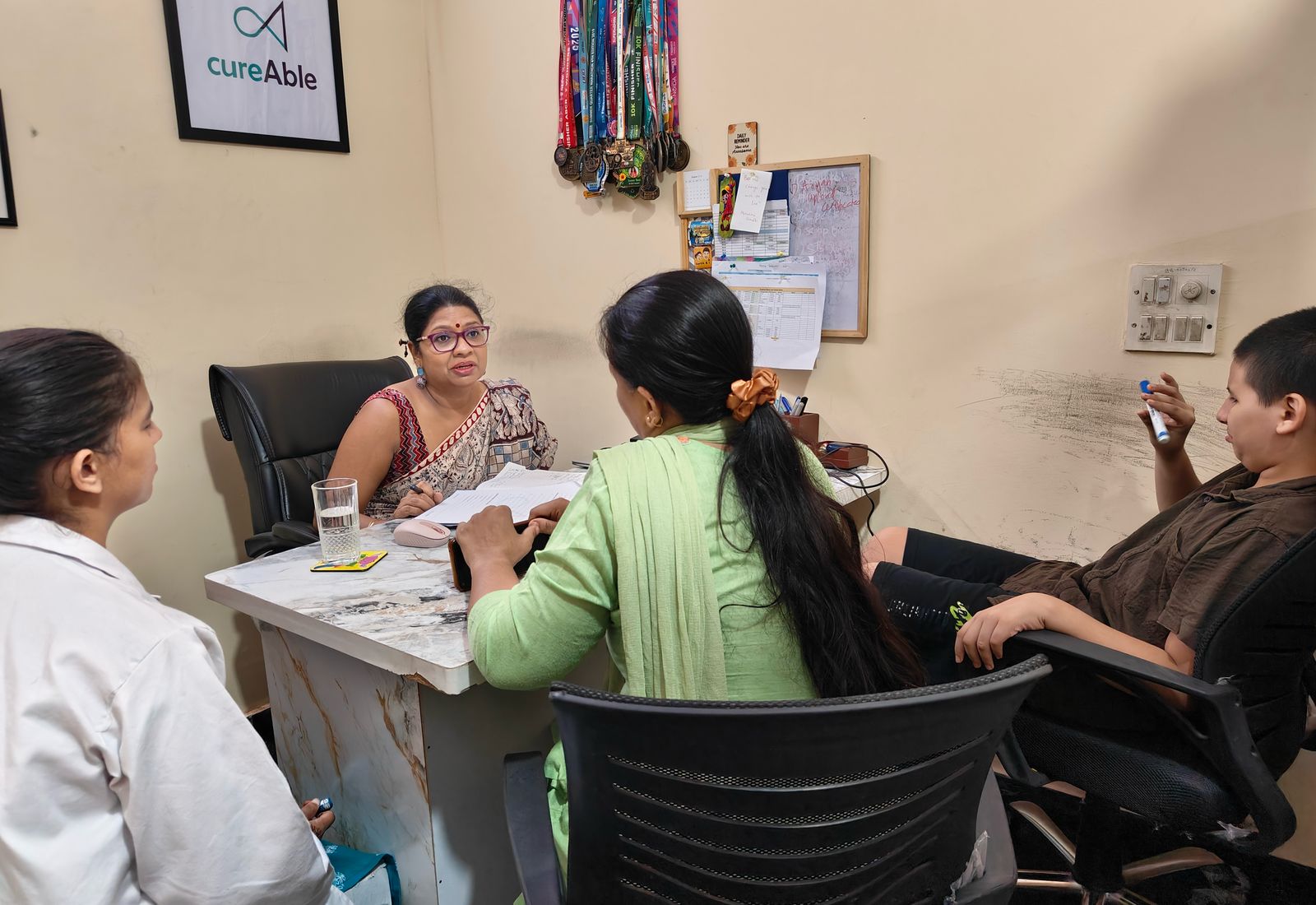 Several adults and a child seated together around one desk in a CureAble consultation room.