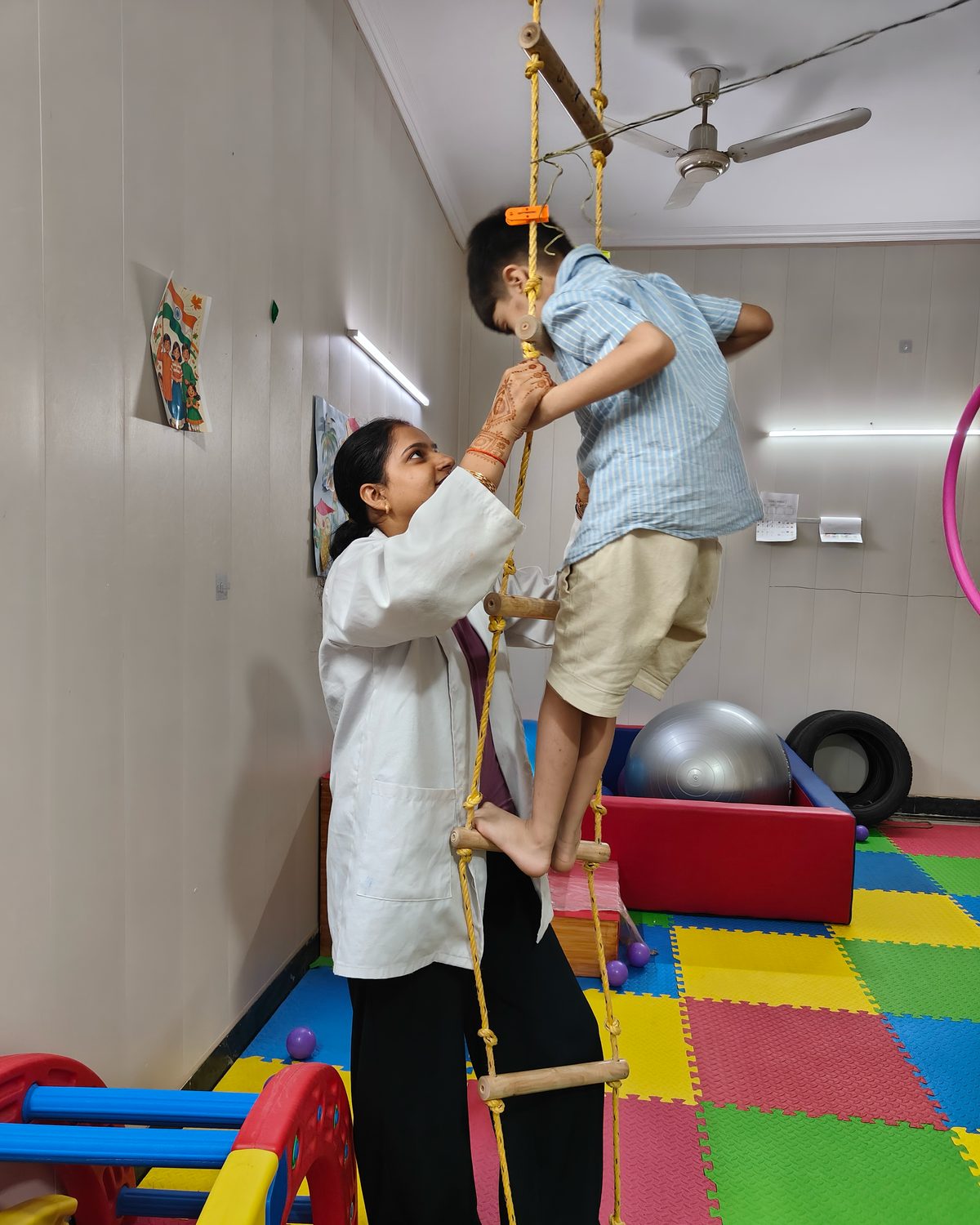A CureAble therapist supports a child climbing a rope ladder in an occupational therapy room at the Noida Centre.