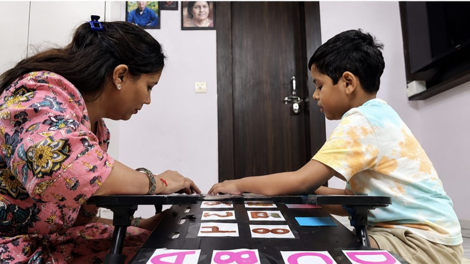 A therapist and a child matching letter cards at a small table at home.