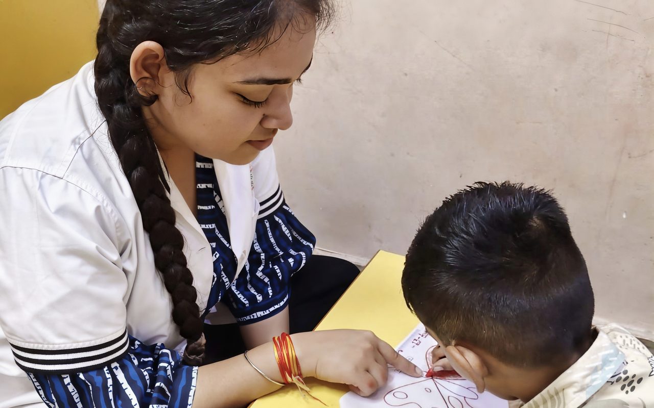 A therapist and a child colouring together at a small table at home.