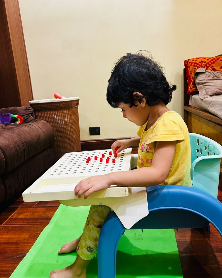 A child seated at a tray table placing pegs into a pegboard.