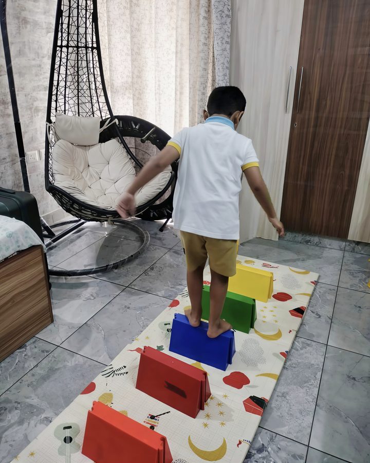 A child stepping across a row of coloured blocks on a floor mat at home.