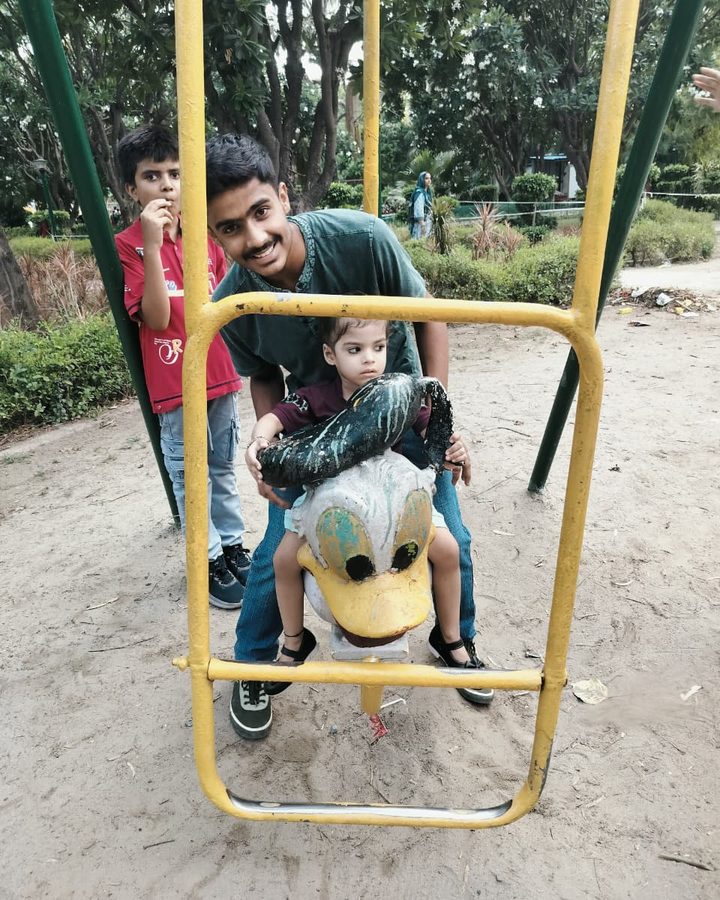 A therapist supporting a child on a swing at an outdoor playground.