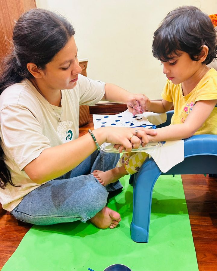 A therapist guiding a child's hand during a tabletop learning activity at home.