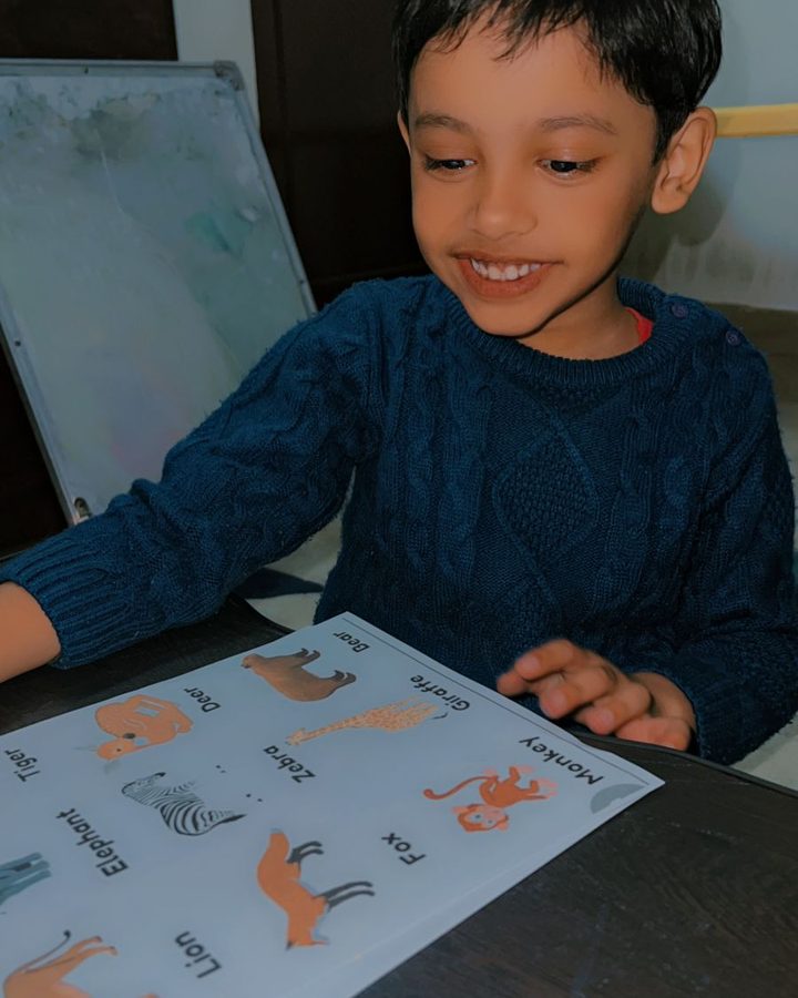 A smiling child pointing to pictures on an illustrated word sheet.