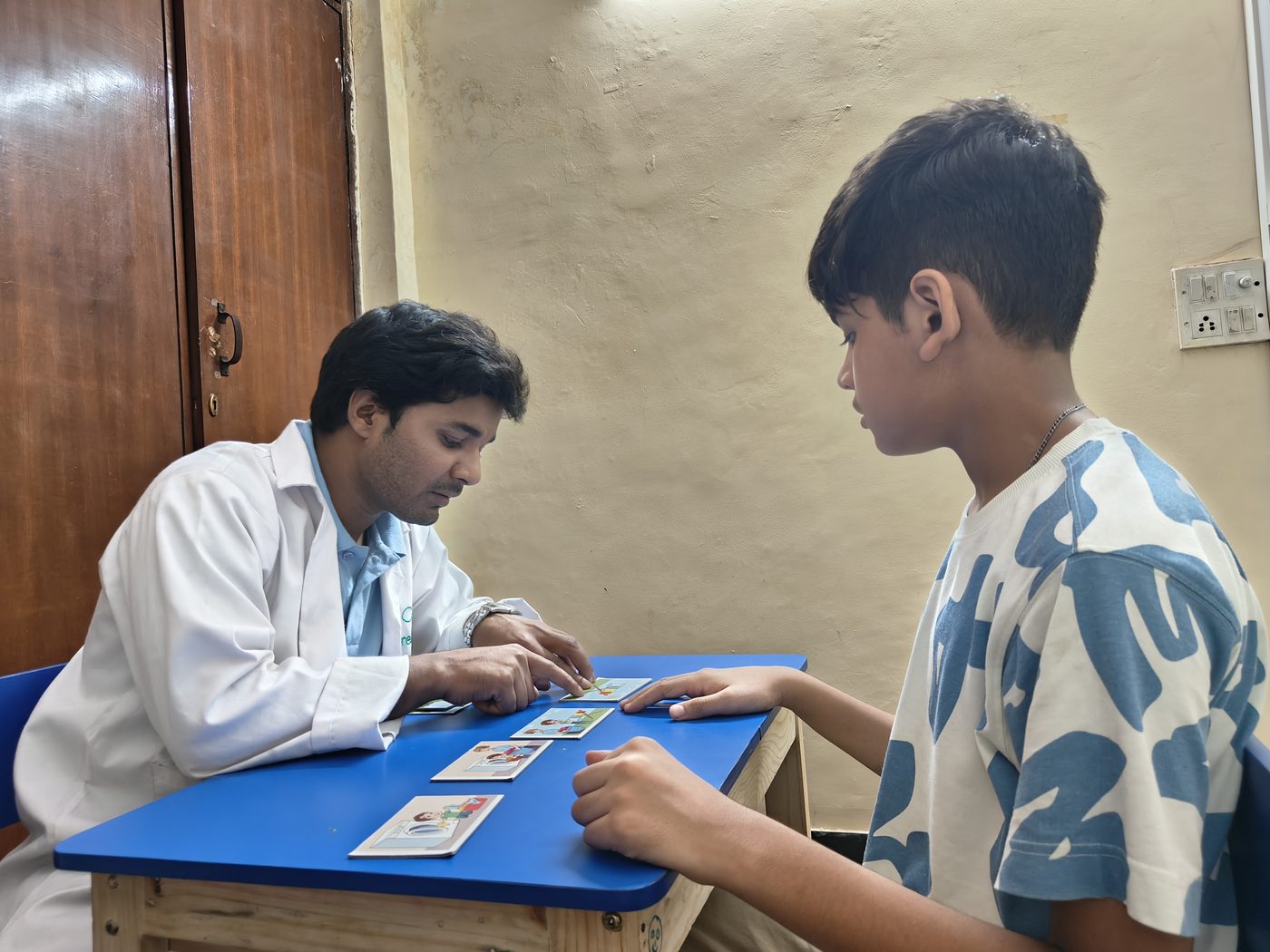 A CureAble therapist and a child work through picture cards at a centre table.