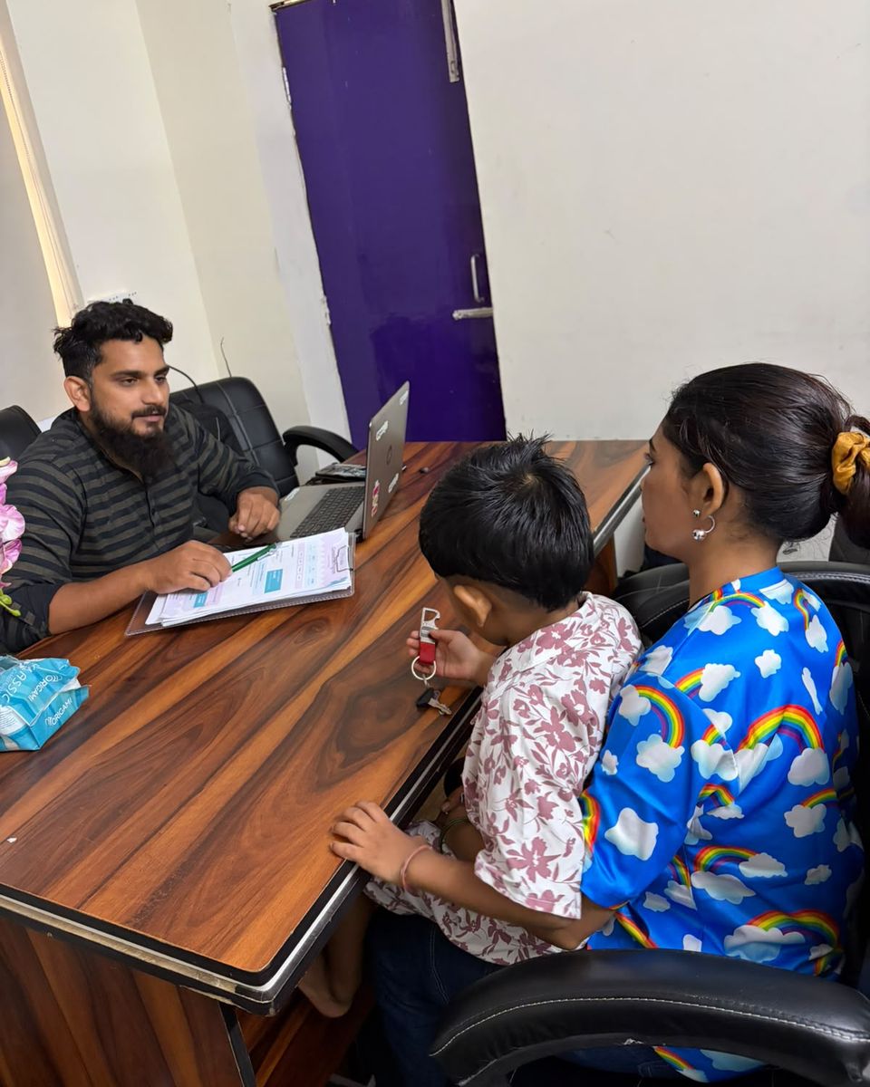 A child and an adult talking with a CureAble counsellor across his desk.