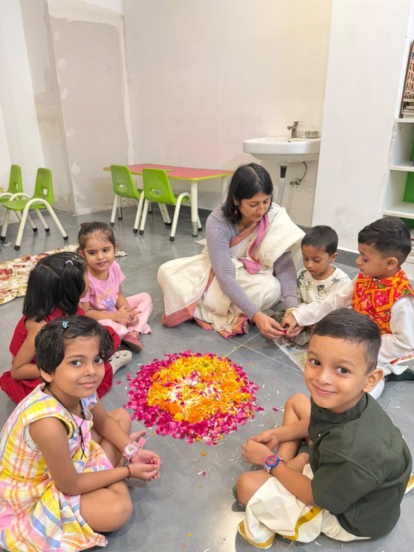 A teacher sitting in a circle with smiling children around a flower arrangement.