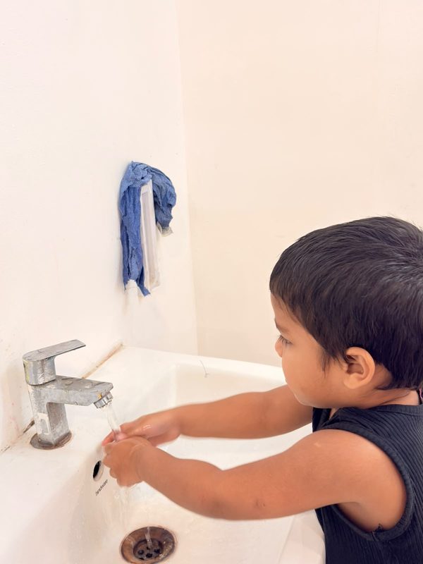 A young boy washing his hands at a low basin.