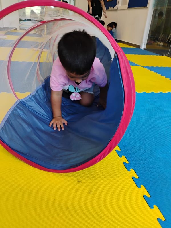 A young child crawling through a fabric play tunnel.