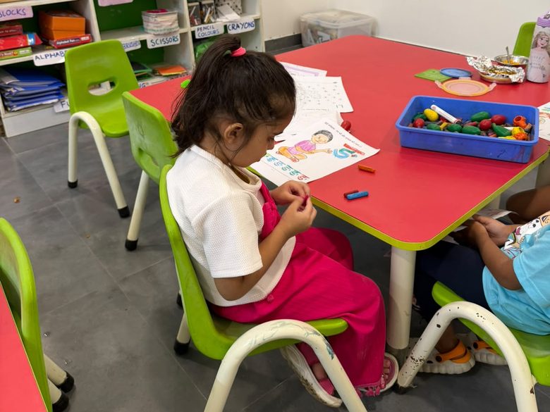 A young girl working with picture sheets and coloured pieces at a classroom table.