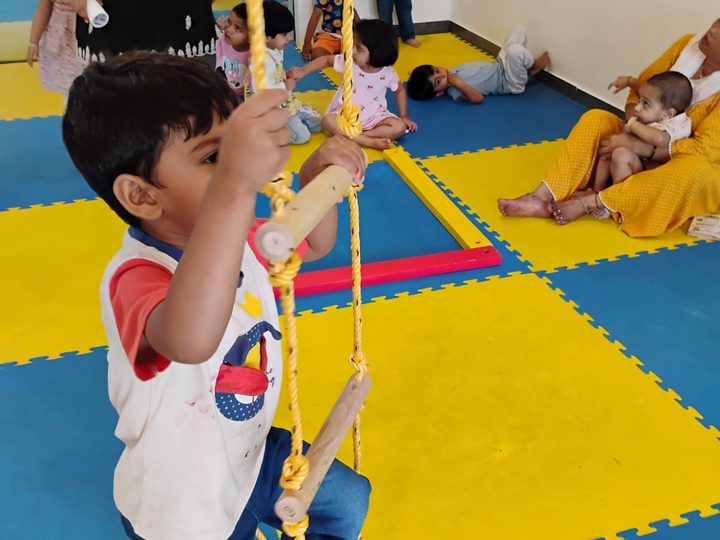 A boy climbing a rope ladder in a play room with soft floor mats.