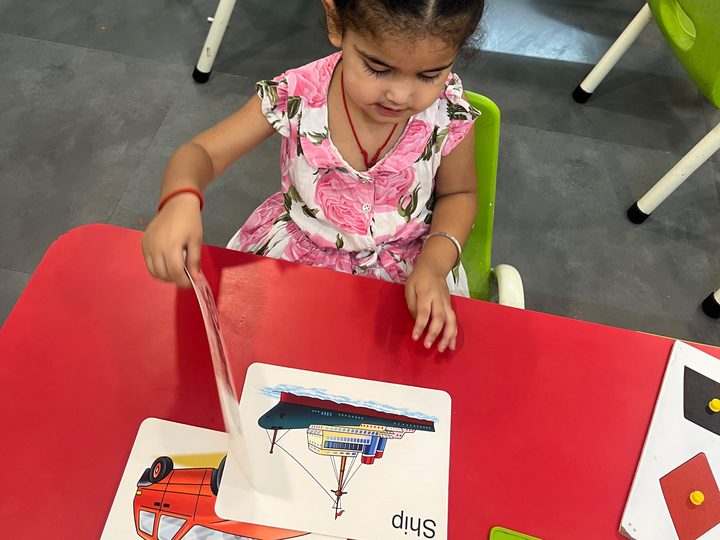 A young girl turning a picture card at a classroom table.