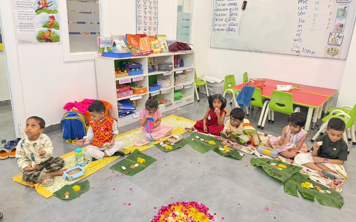 Children sitting on leaf mats on the classroom floor around a flower rangoli.