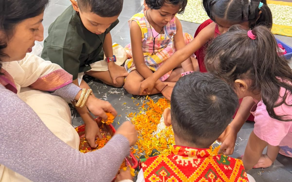 Teachers sitting on the floor with a group of children making a flower arrangement.