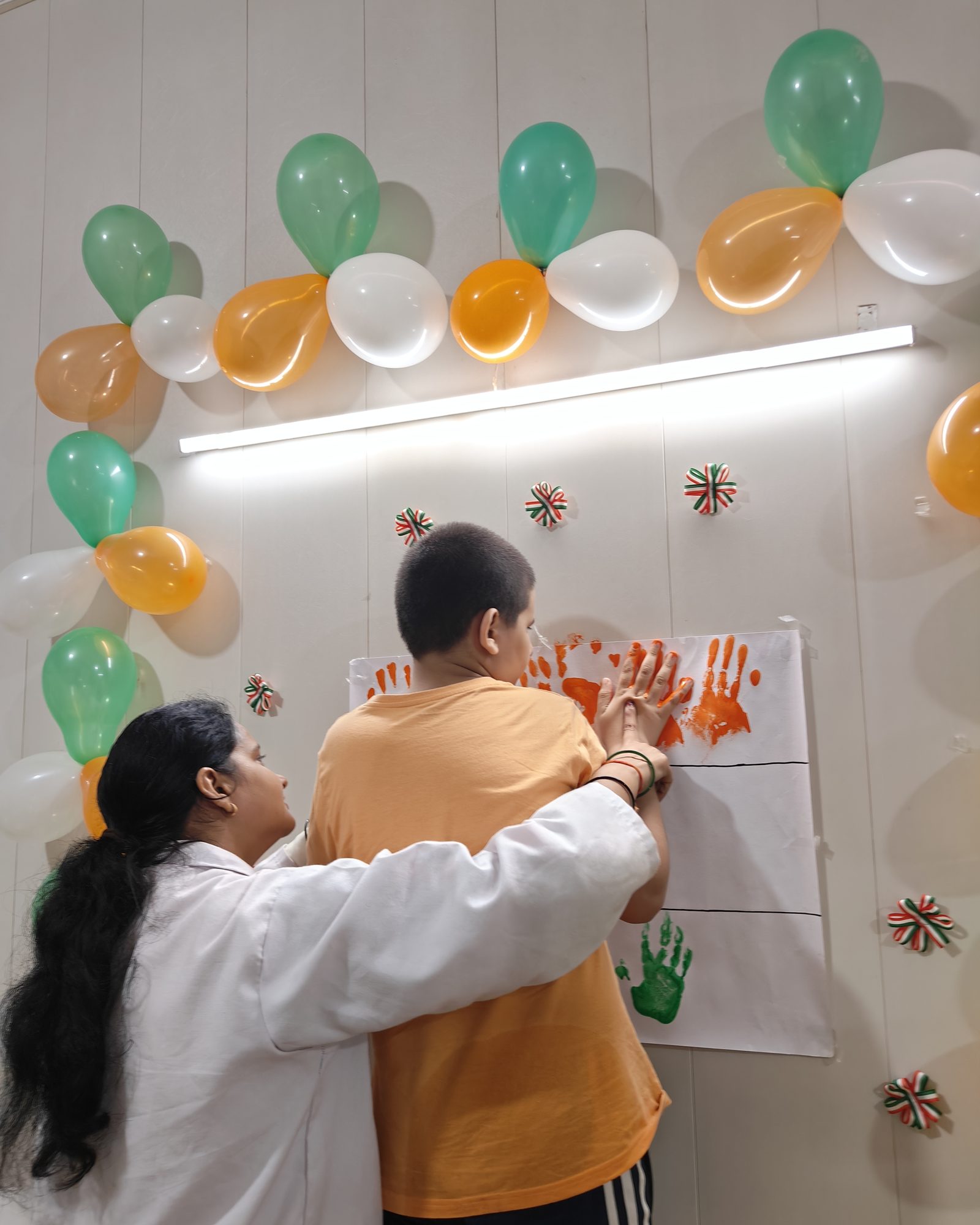 A therapist helping a child press painted handprints onto a festival chart decorated with balloons.
