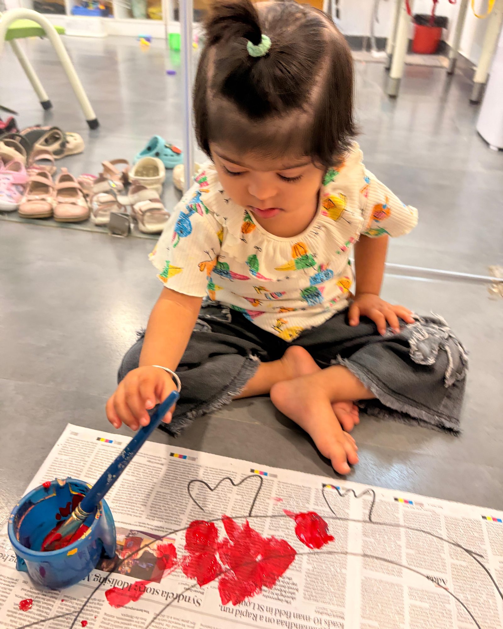 A young child sitting cross-legged on the floor, painting with a brush at EarlyOn.