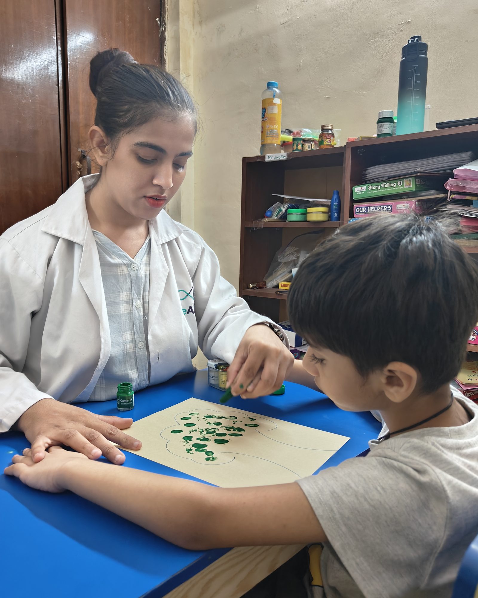 A therapist guiding a child through a leaf-painting activity at a table in a CureAble therapy room.