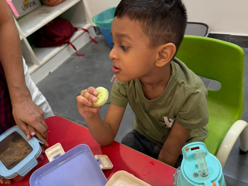 A child eating lunch from his own lunch box at a classroom table.