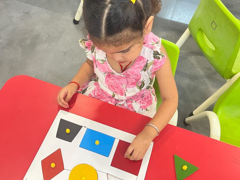 A girl fitting coloured shapes into a puzzle board at a classroom table at EarlyOn.