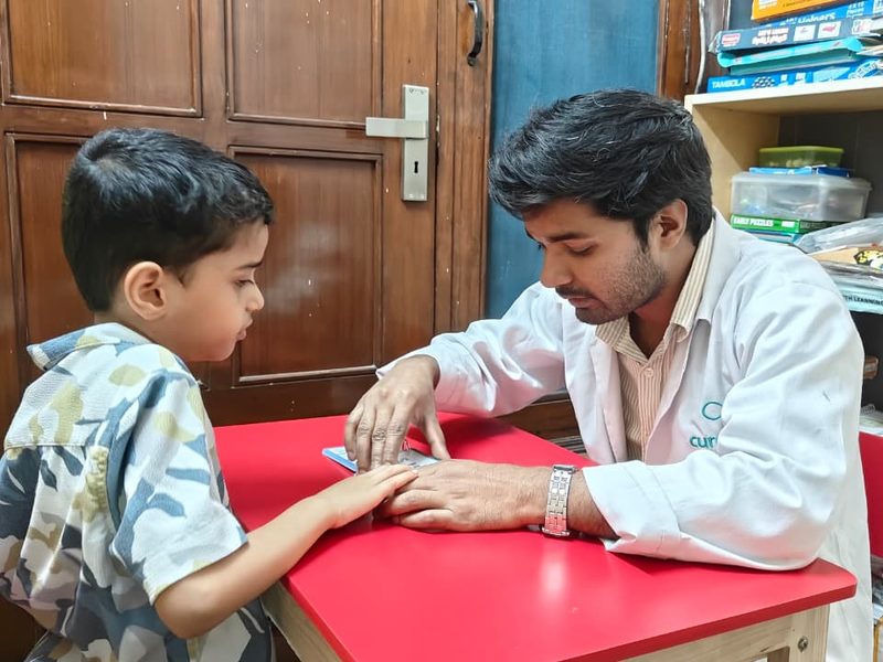 A therapist and a child working with picture cards at a red table at the Noida Centre.