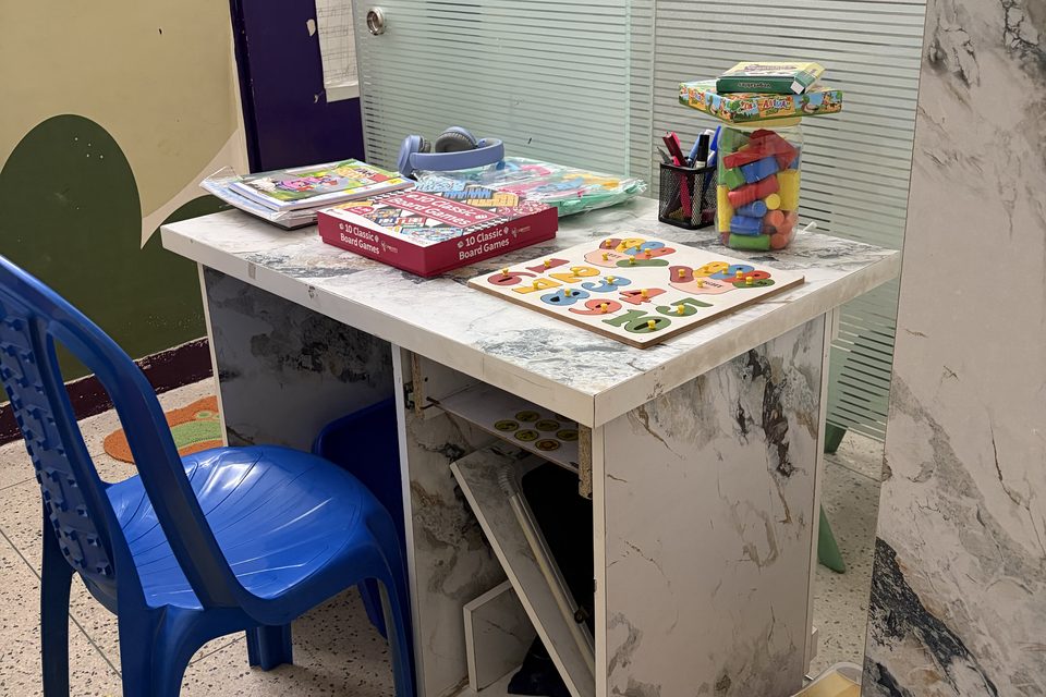 A child-size learning desk with books, puzzles and a blue chair at CureAble Dwarka.