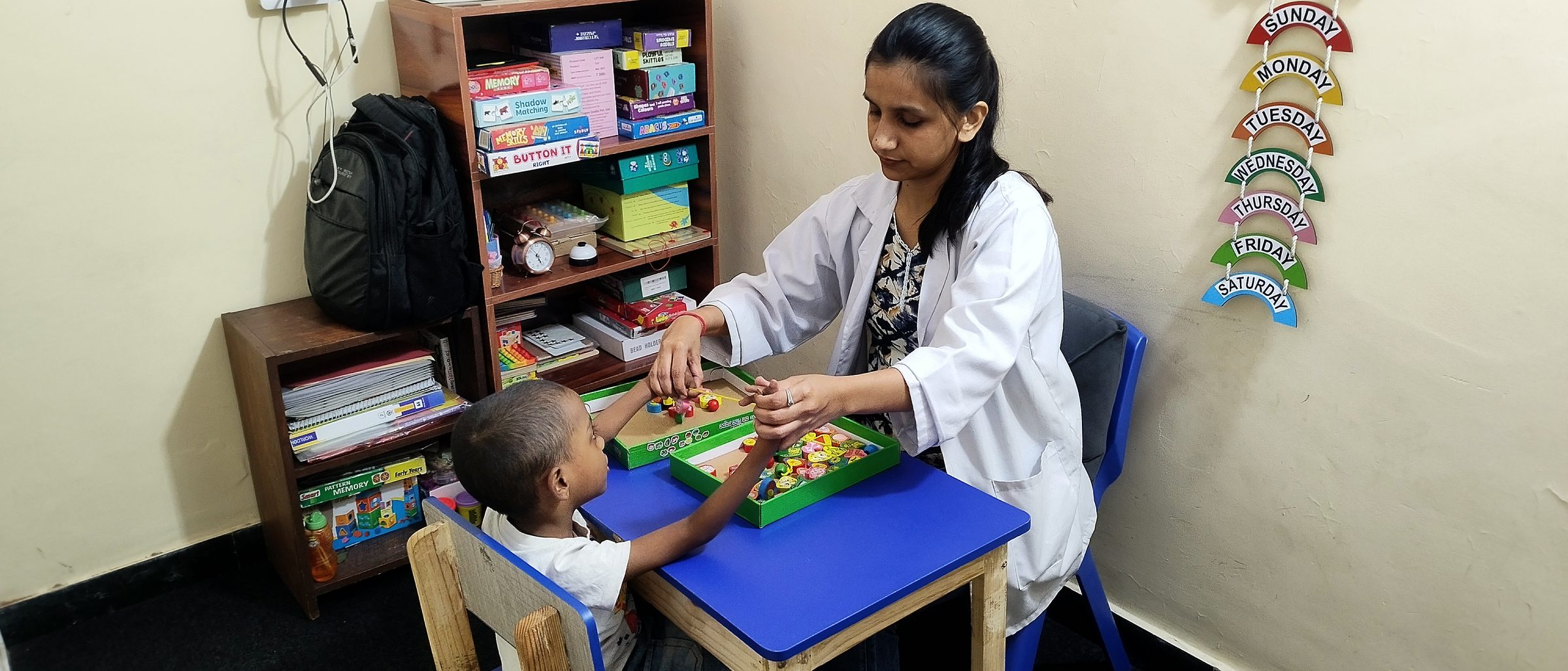 A therapist and a young child sorting coloured pieces together at a small table in a CureAble therapy room.