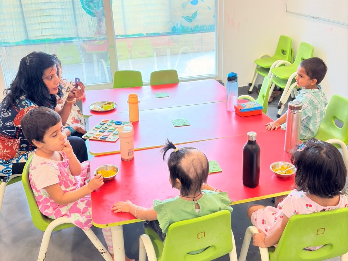 A teacher sitting with young children around a classroom table at lunchtime at EarlyOn.
