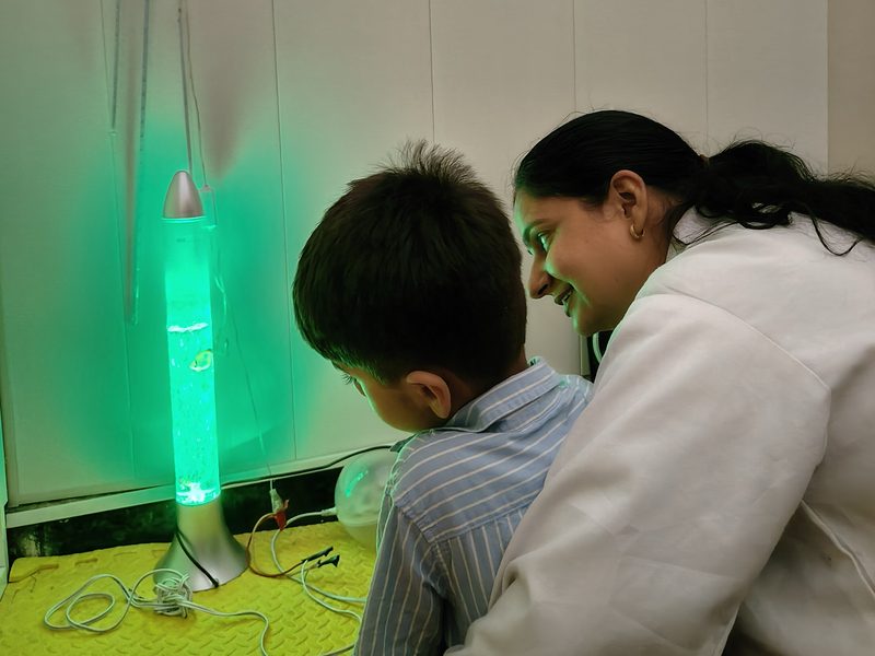 A therapist and a child smiling at each other beside a glowing sensory light.
