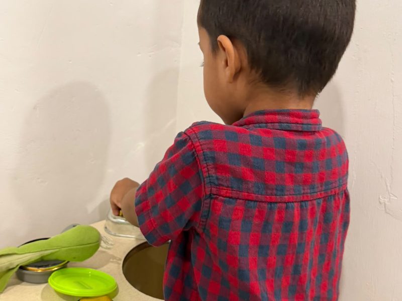 A child playing at a toy kitchen with pots and pans.