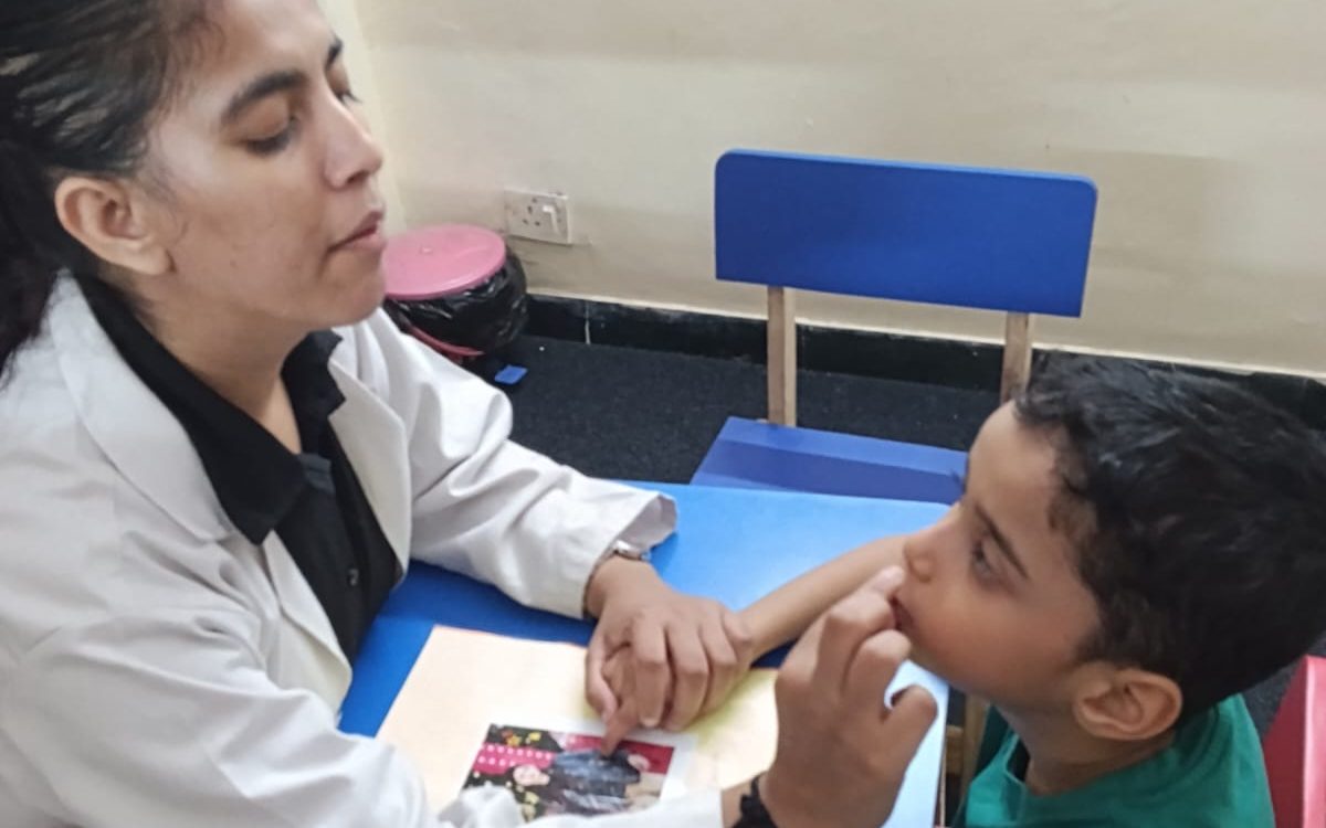 A CureAble speech therapist talking with a child across a small blue table.