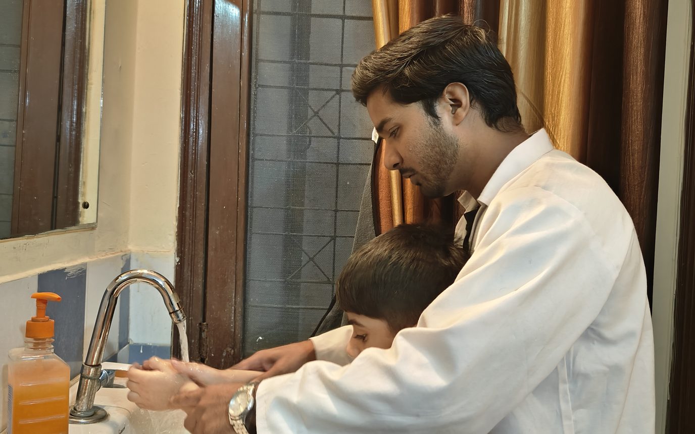 A therapist guiding a child through washing their hands at a basin.