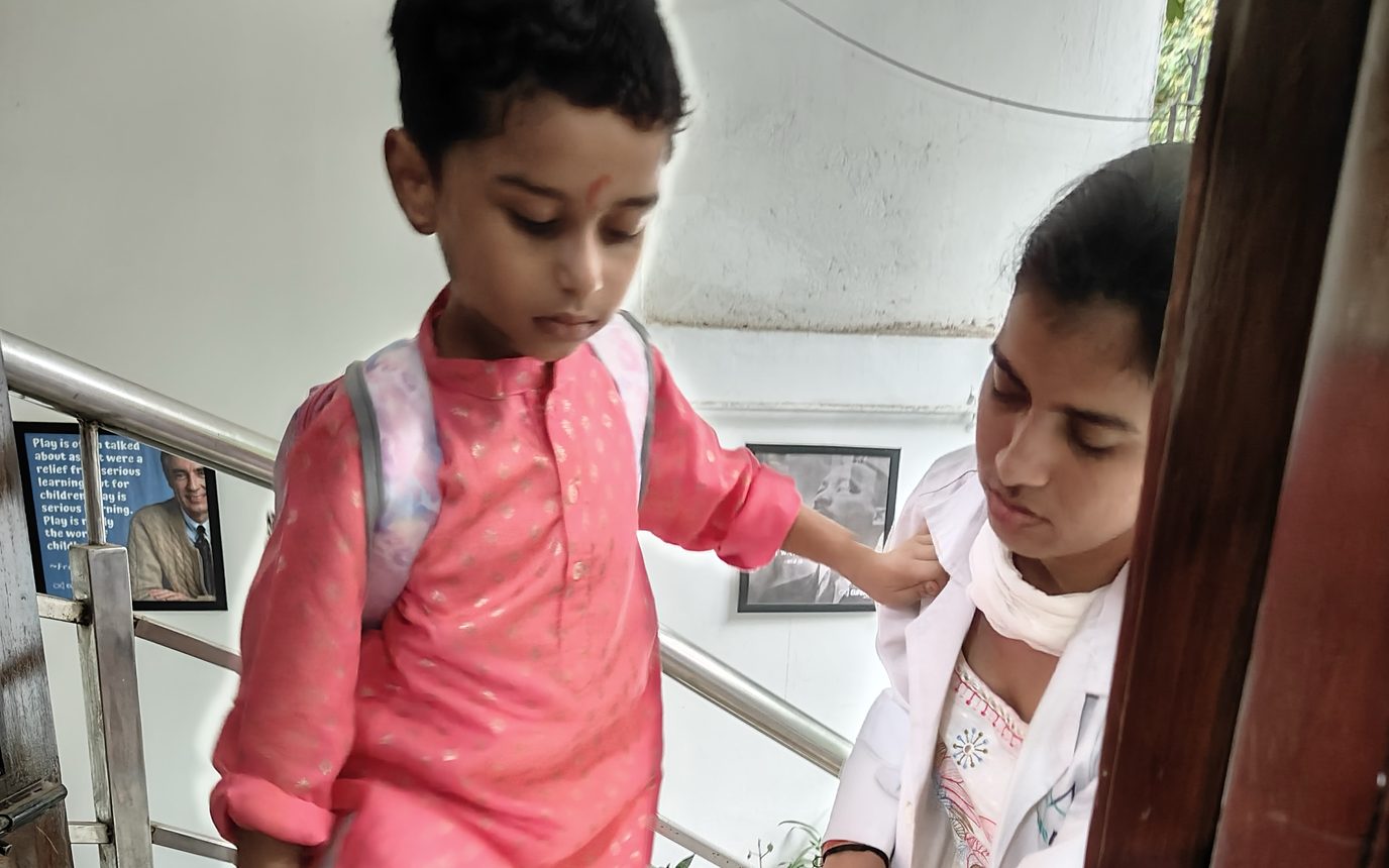 A therapist walking beside a child wearing a school bag as he climbs the stairs at the Noida Centre.