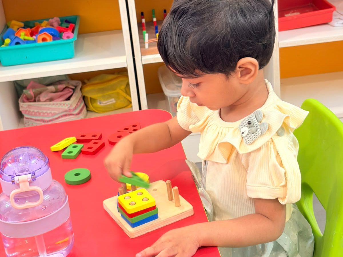 A young child fitting shapes onto a stacking toy at a classroom table at EarlyOn.