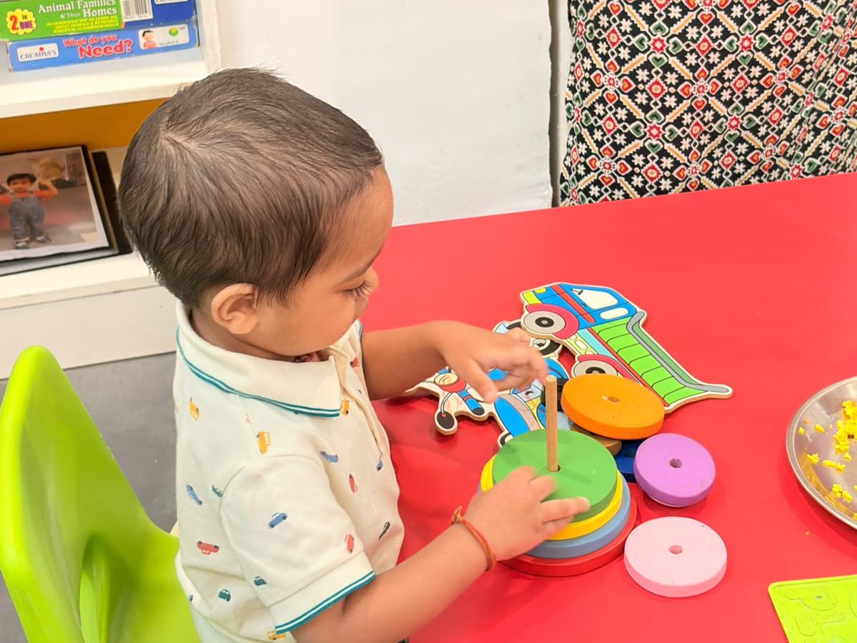 A toddler stacking coloured rings at a classroom table at EarlyOn.