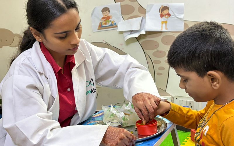 A CureAble therapist helping a child practise eating independently at a small table at CureAble Dwarka.