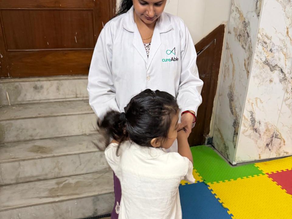 A CureAble therapist holding a child's hands as she balances on a mini trampoline at the Noida Centre.